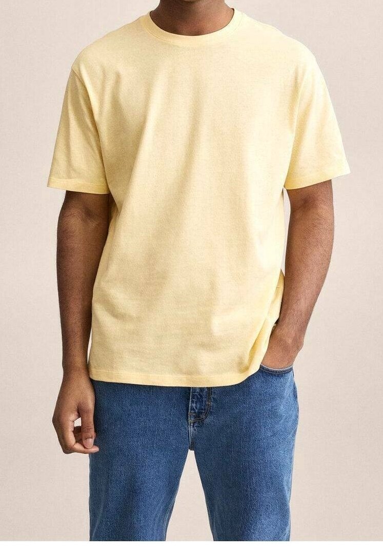 Homme portant un t-shirt jaune clair uni à manches courtes et un jean bleu, une main dans la poche, sur un fond neutre.
