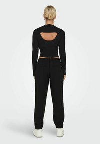 Maglietta nera a maniche lunghe e corta dietro, abbinata a pantaloni neri a vestibilità ampia e sneakers bianche. Tessuto a coste sulla maglietta.
