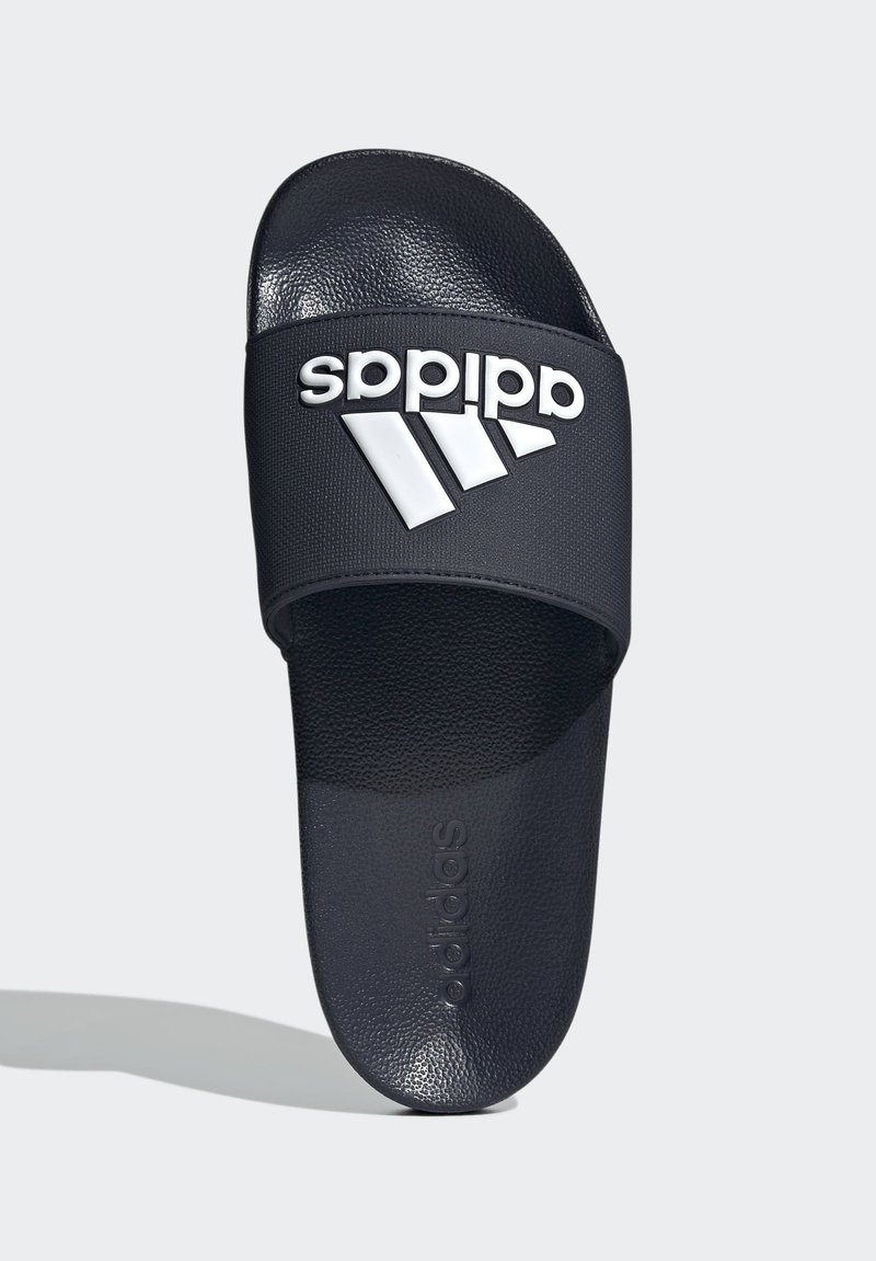 Sandale tip slide negre Adidas cu branț texturat și logo alb pe o curea lată, fotografiate de sus pe fundal deschis.