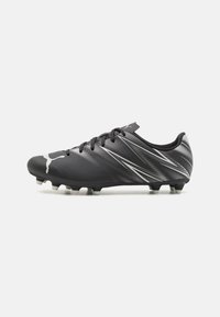 Botas de fútbol negras con una superficie texturizada, rayas diagonales blancas y un diseño elegante. Presenta un cierre con cordones en la parte delantera y una suela con tacos.