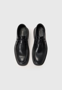 Svarta läderskor med en slät yta, rund tå och kontrasterande tjock gummisula. Har minimal sömnad och snörningsdetaljer.