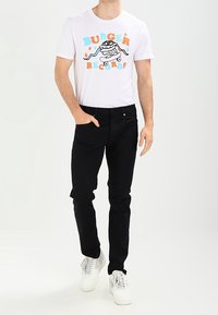White T-shirt with a colorful "Burger Records" graphic, paired with black fitted pants and white sneakers. Minimalist design with a casual fit.