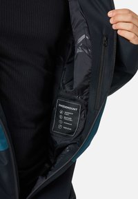 Zwarte waterdichte jas met teal accenten, voorzien van een ritssluiting binnenzak en een label dat de waterdichtheid, ademend vermogen en winddichte eigenschappen toont.