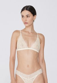 Krajkový bralet a odpovídající thong v světle béžové barvě. Obsahuje jemné květinové vzory a tenké nastavitelné ramínka. Měkká textura a trojúhelníkový tvar.