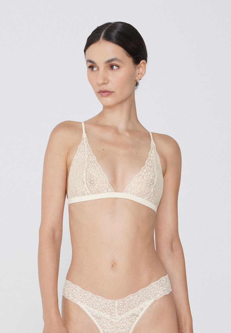 Krajkový bralet a odpovídající thong v světle béžové barvě. Obsahuje jemné květinové vzory a tenké nastavitelné ramínka. Měkká textura a trojúhelníkový tvar.