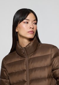 Brązowa kurtka puchowa z wysokim kołnierzem, z pikowanym wzorem i gładką fakturą. Zamek błyskawiczny z przodu, odpowiednia na zimną pogodę.