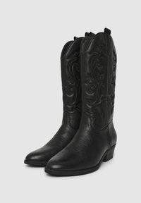 Para czarnych skórzanych kowbojek z dekoracyjnymi haftami i niskimi, grubymi obcasami na szarym tle.