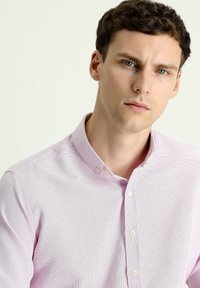 Camisa de botones de color rosa claro hecha de tela texturizada, con cuello y un patrón sutil; presenta pequeños botones y un diseño ajustado.