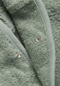 Groene badstof met een gladde rand, voorzien van zilveren drukknoopsluitingen. Zachte textuur met een donzige oppervlakte.