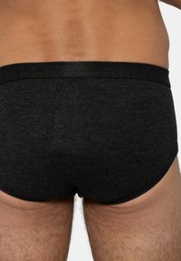 Slip neri a coste con una morbida cintura elastica, design aderente e texture liscia, che mostrano una vista parziale del corpo.