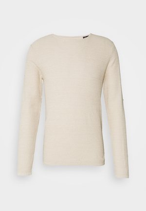 Pull à manches longues et col rond en tissu tricoté texturé beige clair avec un motif côtelé, sans boutons ni ornements visibles.