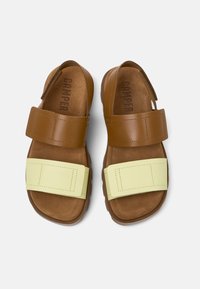 Brown leather sandals with two wide straps; one is brown and the other is light yellow. Soft suede footbed and durable rubber sole.