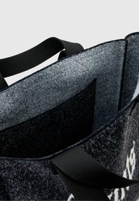 Szara torba na ramię z filcu z czarnymi nylonowymi uchwytami; wnętrze ma miękką teksturę i boczną kieszeń do organizacji. Zauważalny kontrast kolorów.