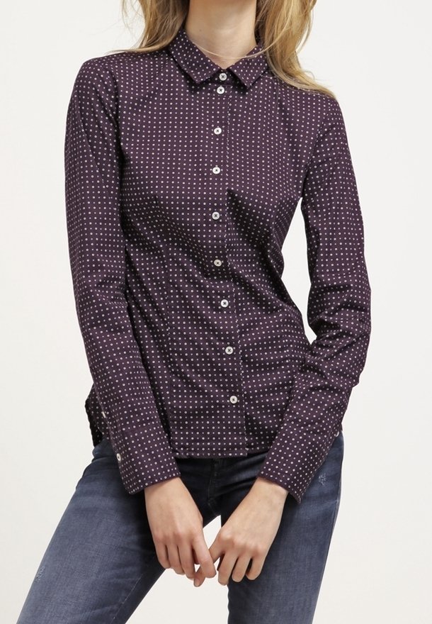 Chemise boutonnée bordeaux à pois blancs, à manches longues, avec col et coupe ajustée, présentant une texture lisse et un style classique.