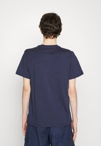 Námořnická modrá bavlněná tričko s kulatým výstřihem a krátkými rukávy, s volným střihem a minimalistickými švy. Hladký zadní pohled.