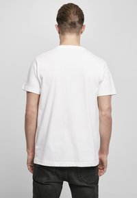 Hvit bomull t-skjorte med korte ermer og rund hals, vist fra baksiden, enkel design, ingen grafikk eller mønstre synlig.