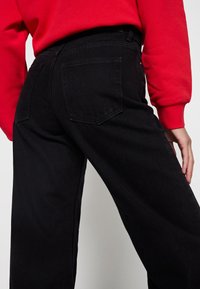 Svarta denimbyxor med hög midja, med bakfickor och en lös benprofil. Matchas med en ljusröd sweatshirt.