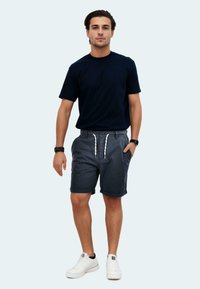 Marineblaues T-Shirt mit kurzen Ärmeln, kombiniert mit grauen Shorts mit elastischem Bund und Kordelzug. Weiße Sneakers runden den Look ab.