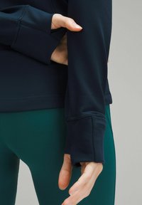 Marineblauw langemouwen top met een getailleerd ontwerp, voorzien van een zachte textuur en duimgatenmanchetten, gecombineerd met groene high-waisted leggings.