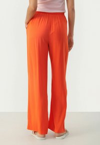 Kraftige orange bukser med vidde, elastisk talje og sidelommer, lavet af et glat og let stof.