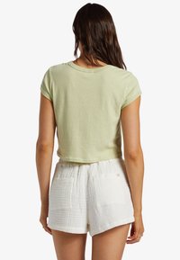 Jasnozielona krótka koszulka z krótkimi rękawami, gładka w dotyku, z okrągłym dekoltem, zestawiona z białymi szortami o fakturze, posiadającymi kieszenie.