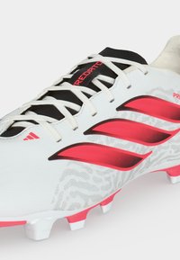 Λευκό ποδοσφαιρικό παπούτσι Adidas με ροζ ρίγες, μαύρη γλώσσα, λευκά κορδόνια και ροζ καρφιά στη σόλα.
