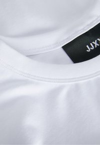 Vit bomullströja med rund halsringning och mjuk textur. Har en svart etikett med vit text på insidan av kragen.