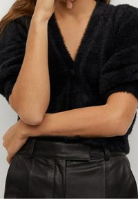 Maglione nero peloso con scollatura a V profonda, caratterizzato da una morbida consistenza e maniche voluminose, abbinato a pantaloni in pelle nera a vita alta.