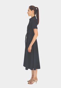 Granatowa sukienka koszulowa z krótkimi rękawami, z talią ściąganą i spódnicą do kolan. Posiada kołnierzyk i gładkie wykończenie materiału.