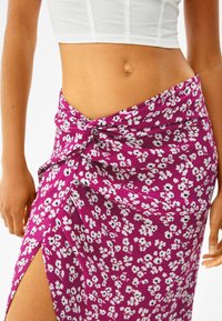 Lila blommig omslagsskjol med knutdetalj i midjan, kontrasterande vita och svarta blommönster, mjukt tyg och en högt skår.