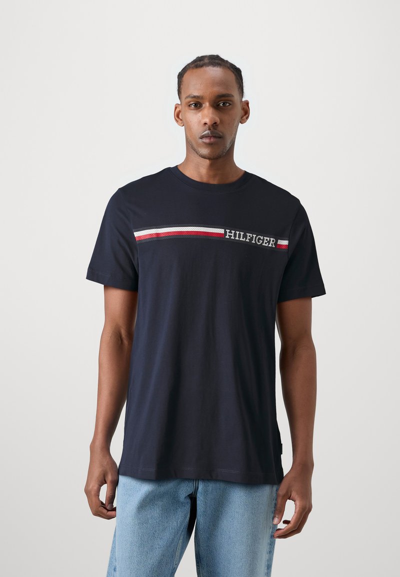 Tricou din bumbac bleu marin, cu mâneci scurte, având un accent orizontal în dungi roșii și albe, cu textul "HILFIGER" brodat în alb.