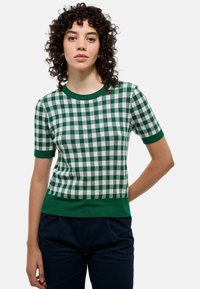 Pull à manches courtes à carreaux verts et blancs avec un col rond et des bords côtes au niveau des poignets et de l'ourlet, en tissu tricoté.