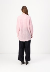 Ulløs rosa genser med avslappet passform, lange ermer og avrundet kant, kombinert med vide, mørke stripete bukser og svarte hæler.