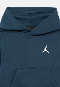 Φούτερ με κουκούλα σε σκούρο τιρκουάζ, ύφασμα από μείγμα βαμβακιού. Διαθέτει τσέπη καγκουρό και λευκό λογότυπο Jordan στο στήθος. Λείο υφή.