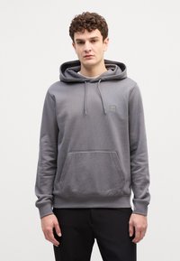 Šedá mikina vyrobená z měkké tkaniny, s velkou přední kapsou, šňůrkami na stažení a malou nášivkou značky na hrudi. Design je jednoduchý a neformální.