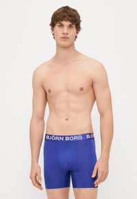 Boxer briefs azuis feitos de um tecido suave com uma banda branca com o logótipo "BJÖRN BORG" na cintura. Design justo, com comprimento até a meio da coxa.