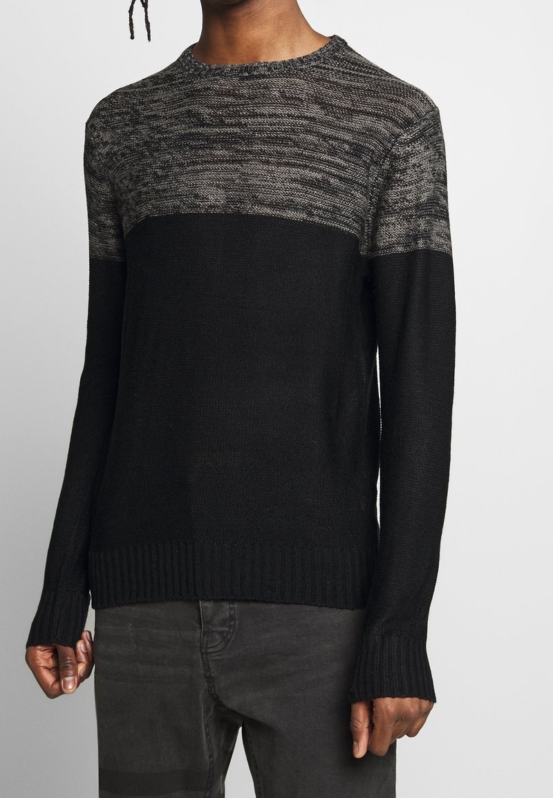 Czarny dziany sweter z szarą teksturowaną górą, wykończony prążkowanym ściągaczem u dołu i na rękawach. Materiał jest miękki i lekki. Długie rękawy.