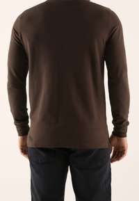 Pitkähihainen ruskea paita pehmeää kangasta, jossa on pyöreä pääntie ja sivuhalkiot. Yhdistetty tummiin farkkuihin, joka antaa rentoa ilmettä.