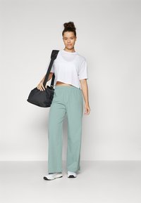 T-shirt bianco accorciato, pantaloni larghi verde chiaro e borsa nera. Il modello indossa sneakers bianche. Tessuti morbidi e vestibilità rilassata.