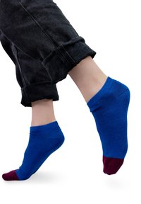 Niebieska skarpetka do kostek z winobranżowym piętą i palcami, wykonana z miękkiego materiału. Nosi się ją z podwiniętymi czarnymi dżinsami, co podkreśla kontrast kolorów i dopasowanie.