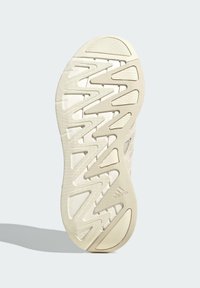 Sula av träningsskor i ljusbeige, med vinkelräta mönster och texturerade ytor för grepp. Adidas-logotyp på sidan.