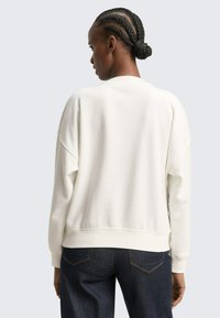 Witte, gestructureerde sweatshirt met een losse pasvorm, geribbelde manchetten en een ronde hals. Draagt donkere spijkerbroek en straalt een casual stijl uit.