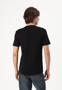 Svart kortärmad T-shirt i bomull. Rundad hals med en mjuk textur. Sedd bakifrån, med minimal detaljering.