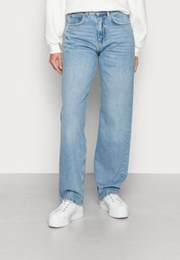 Ljusblå denimjeans med rak bendesign, hög midja och subtila blekningar. Kombineras med vita plattformssneakers.