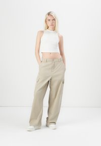 Beiga cargo byxor med stora sidofickor, tillsammans med en vit, åtsittande, ärmlös crop-top. Skorna är vita sneakers. Minimalistisk design.