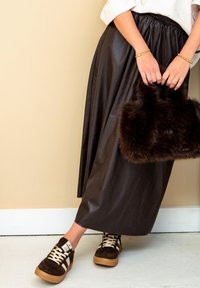 Bruine leren maxi-rok met een elastische tailleband, gecombineerd met een bruine nepbont handtas en donkere sneakers met witte accenten.