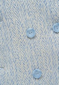 Hellblaues und cremefarbenes Fischgrätenmuster aus einem strukturierten Gewebe, mit runden hellblauen Knöpfen im Zweilochdesign.