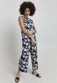 Ensemble deux pièces avec un fond bleu marine et des motifs floraux blancs. Le haut a des manches à volants ; le look est complété par un pantalon large.