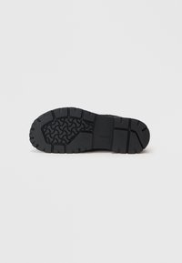 Sole di stivale in gomma nera con scanalature profonde e motivi curvi su uno sfondo bianco neutro.