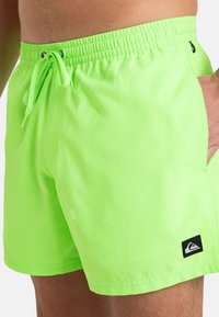 Bañadores verdes neón con cinturilla elástica, cordón y bolsillo lateral. Incluye un pequeño parche con el logo en el costado.